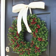 a christmas wreath on the front door with white ribbon hanging from it's side