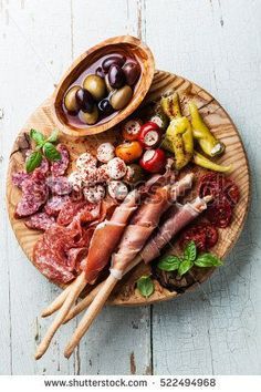 an assortment of meats and vegetables on a wooden platter with olives, tomatoes, pepperoni, peppers, pickles