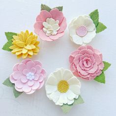 six felt flowers arranged in a circle on a white surface