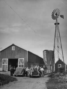 an old black and white photo of people standing in front of a barn with a windmill