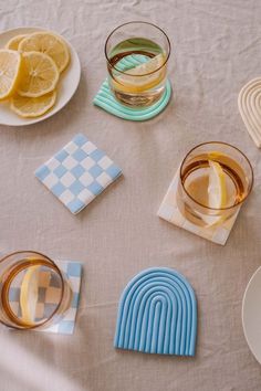 there are several glasses and plates on the table with lemons, gingham paper napkins, and coasters