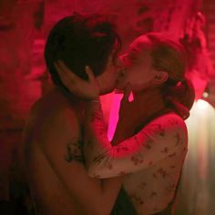 a man and woman kissing each other in front of a red light with their arms around them