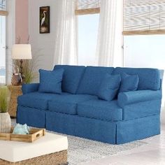 a living room with blue couches and white curtains on the window sill, in front of an ocean view