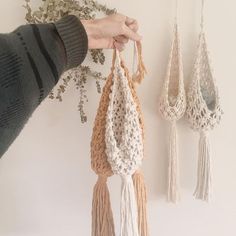 three crocheted tassels hanging from hooks on a wall with flowers in the background