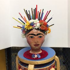 a ceramic head with colorful sticks sticking out of it's face sitting on top of two stools