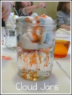 two children are sitting at a table with jars full of food and one child is holding a spoon