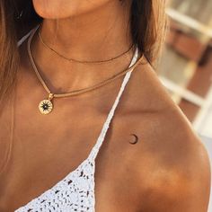 a woman wearing a white top with a sun and moon tattoo on her chest,