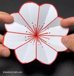 two hands holding up a paper flower with red lines on it's center and the petals are folded in half