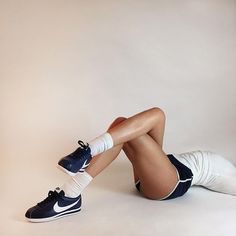 a woman is sitting on the floor with her legs crossed and wearing tennis shoes,