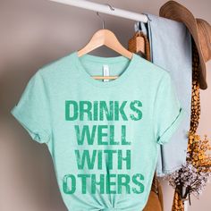 Drinks Well With Others This funny st Patricks Day shirt is everything you’ve dreamed of and more. It feels soft and lightweight, with the right amount of stretch. It’s comfortable and flattering for both men and women. This distressed st patttys day shirt is one of Bella Canvas most popular tees. Graphic: * printed with non toxic vegan ink bonds with garment fibers meaning no peeling *100% combed and ring-spun cotton (heather colors contain polyester) * Color garments have a vintage/ muted appe St Pattys Day Shirts Women, Green Summer Shirt With Slogan, Funny Green Tops With Letter Print, Funny Green Top With Letter Print, Fun Slogan Shirt With Relaxed Fit, Fun Relaxed Fit Slogan Shirt, Relaxed Fit Fun Slogan Shirt, Funny Text Print Shirt For Spring, Green Funny Tops With Text