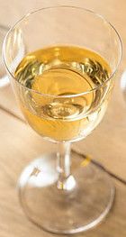 a glass filled with white wine on top of a wooden table next to an orange slice