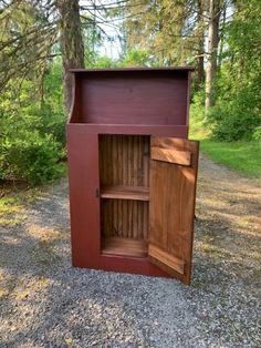 a wooden cabinet sitting on top of a gravel road next to trees and grass in the woods