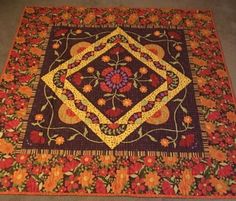 a quilted table runner with an intricate design on the front and center piece in yellow, red, orange, and purple colors