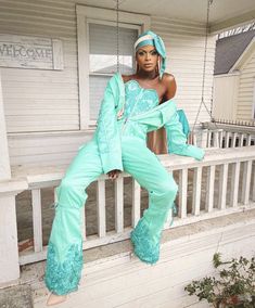 a woman sitting on a porch with her legs crossed and wearing turquoise clothing, posing for the camera