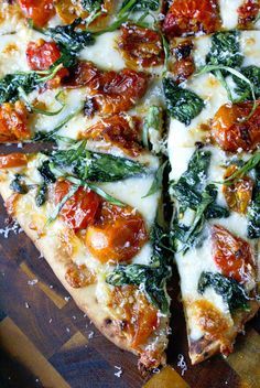 a pizza with tomatoes, spinach and cheese on a cutting board