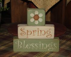 a wooden block sign that says spring is blooming on top of a plaid table cloth