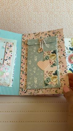 a hand holding an open book with flowers and hearts on the pages, in front of a wallpapered background