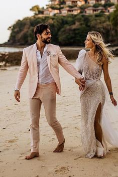 a man and woman walking on the beach holding hands, dressed in wedding attire with high slit skirt