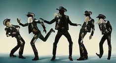 four people dressed in black and gold are dancing with hats on their heads, arms and legs