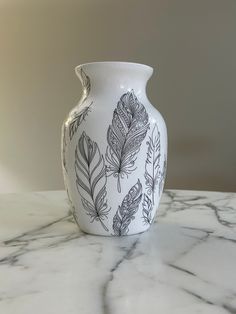 a white vase sitting on top of a marble counter covered in black and white feathers