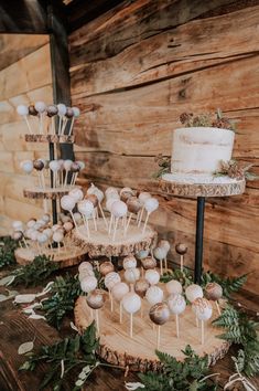 wedding cake and desserts displayed on wooden slices with greenery in front of wood paneled wall