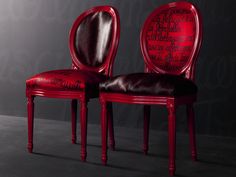 two red chairs sitting next to each other in front of a black wall with writing on it