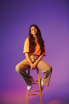 a young woman sitting on top of a wooden stool in front of a purple background