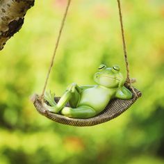 a green frog sitting in a hammock hanging from a tree