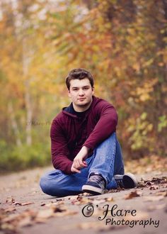 a young man is sitting on the ground in front of trees with leaves all around him