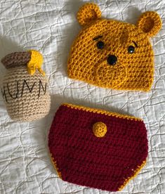 two crocheted items are laying on a white sheet and one has a bear hat