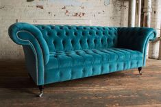 a teal colored couch sitting on top of a wooden floor next to a brick wall