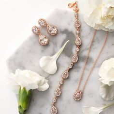 three pieces of jewelry sitting on top of a marble table next to flowers and white carnations