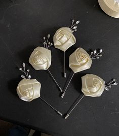 four white roses are sitting on top of a black table next to some silver pins