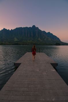 a woman walking on a dock into the water at sunset with mountains in the background