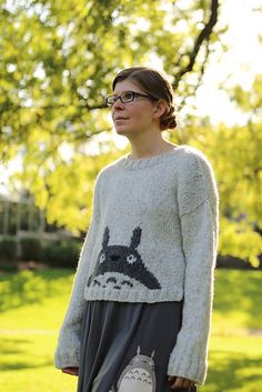 a woman standing in the grass wearing a sweater with an image of a cat on it