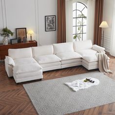 a white sectional couch sitting on top of a hard wood floor next to a window