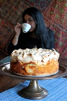 a woman sitting at a table with a cake and cup in front of her face