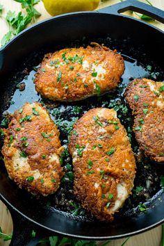 four pieces of chicken in a skillet with parsley on the side and lemon wedges next to it