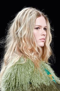 a woman with long blonde hair wearing a green jacket and looking off to the side