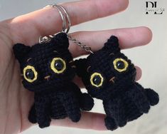 two small black cats with yellow eyes are on a keychain in someone's hand