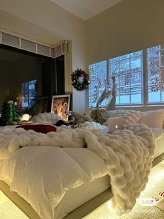 a large bed covered in white blankets next to two windows with christmas decorations on them