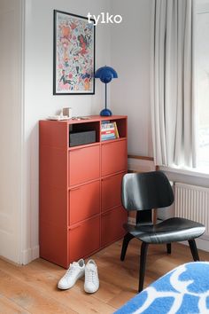 a bedroom with an orange dresser next to a black chair and white shoes on the floor