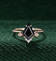 a black diamond ring sitting on top of a green cloth with diamonds around it's edges