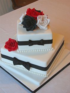 two tiered wedding cake decorated with roses and black ribbon, on top of a table