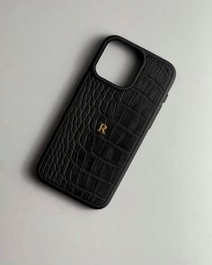 an iphone case with the letter r in gold on black crocodile skin, sitting on a white surface