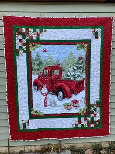 an old red truck with christmas decorations on it is hanging from the side of a house