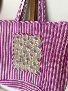 This handmade quilted market bag is fully reversible! This boho tote features a sage green and pinkish purple floral print on one side and a pink and white stripe print on the other. Made of soft yet sturdy natural cotton fabric, this floral market bag features a convenient open top and a large pocket to stash your things! Take this boho tote to the local Farmer's Market, carry it as your everyday bag or even use it as an elevated beach bag! Floral Market Bag Highlights: Measures 14 inches in height and 22 inches in width Large Pocket Two over the shoulder/carry straps 100% Super Soft Cotton Non-Toxic Materials Carbon neutral production Sustainably and Ethically sourced, and Fair trade This boho tote from The Fox and the Mermaid is artisan hand block printed in India using a centuries old Bohemian Reversible Cotton Bag, Purple Bohemian Bags For Spring, Purple Cotton Tote Bag, Pink Floral Print Cotton Bag, Rectangular Cotton Shoulder Bag With Floral Print, Purple Cotton Tote Shoulder Bag, Rectangular Cotton Floral Print Shoulder Bag, Purple Rectangular Cotton Shoulder Bag, Rectangular Purple Cotton Shoulder Bag