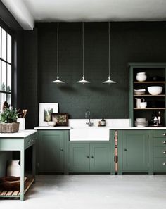 a kitchen with dark green cabinets and white counter tops, along with hanging lights above the sink