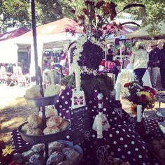 a table topped with cakes and pastries under a canopy covered in flowers on top of a lush green field