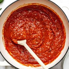 a sauce in a pan with a wooden spoon on the side next to some basil leaves